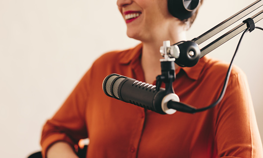 Happy woman smiling and looking away while sitting behind a microphone with headsets. Cheerful woman interviewing a guest while hosting a live radio show in a broadcast studio.