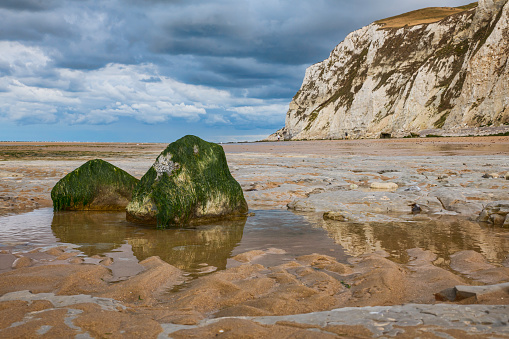 two large stones with algae on the beach of the chalk cliffs of cap blanc nez in france with dark clouds of thunder and rain, part of normandy where the war was fought