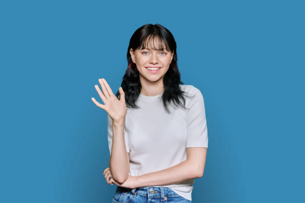 istock Friendly young woman waving hand in greeting, over blue background 1464751966