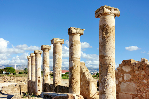 PAPHOS, CYPRUS - January 29 2023: Columns and structures are part of the ancient romans ruins in Paphos Archaeological Park - Cyprus. At the background the lighthouse This site is an UNESCO World Heritage site