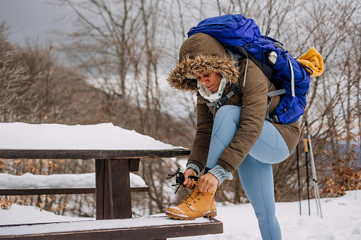 Woman hiker with a backpack on her back is tying her shoelaces