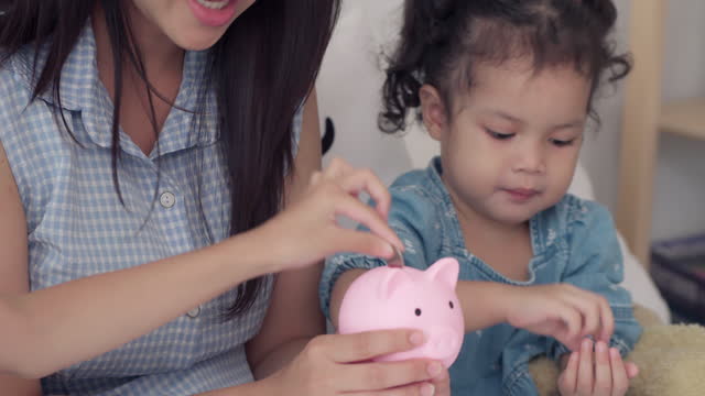 Close up hand Asian baby girl putting a coin in to piggy bank