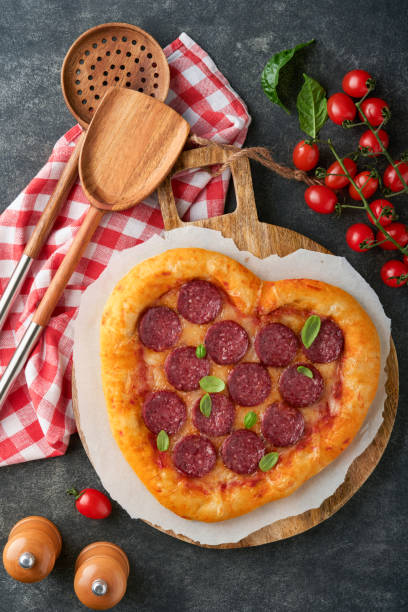 istock Valentines day heart shaped pizza with mozzarella, pepperoni and basil, wine bottle, two wineglass, gift box on black background. Idea for romantic dinner Valentines day. Top view. Mock up. 1464754543