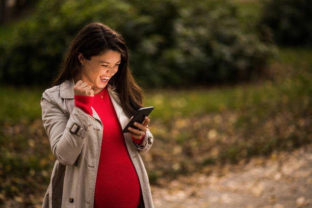 istock Ecstatic young pregnant woman using phone outdoors. 1464754958