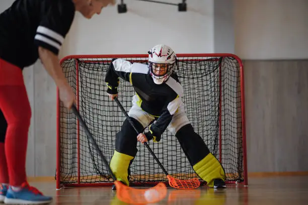 A close-up of woman floorball goalkeeper in helmet concetrating on game in gym.