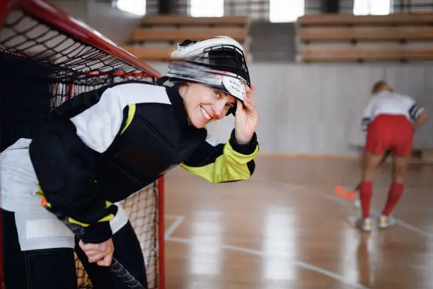 A close-up of woman floorball goalkeeper in helmet concetrating on game in gym.