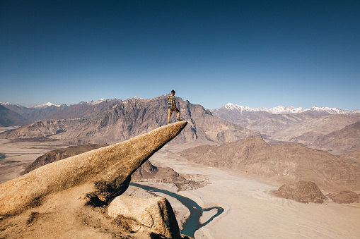 The male traveler on the Marsur Rock looking at the scenic view of Indus River valley in the Himalayas mountains in Pakistan