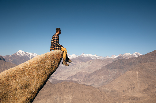 The male traveler sitting at the edge of the cliff in the Marsur Rock and looking at scenic view of  the Indus River valley