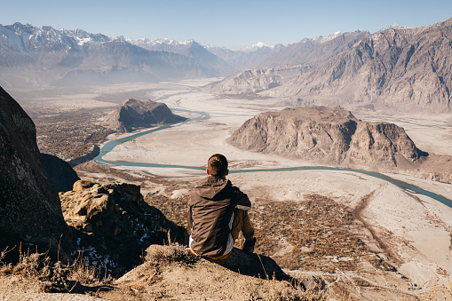 The man traveler sitting and looking at scenic view of the Indus River valley from above in the Himalayas mountains in Skardu, Pakistan
