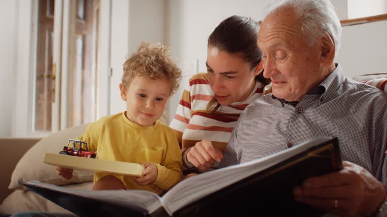 Portrait of a Small Family of Mother, Son, and Grandfather Watching a Photo Album in the Living Room. Family Generations Connecting and Bonding by Spending Time Together, Discussing and Having Fun