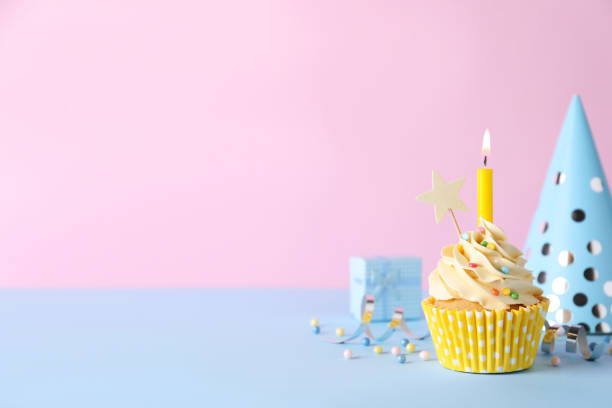 istock Delicious birthday cupcake with burning candle, party decor and gift box on light blue table against pink background, space for text 1464770174