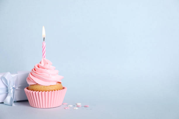 istock Delicious birthday cupcake with burning candle, sprinkles and gift box on light blue background, space for text 1464770177