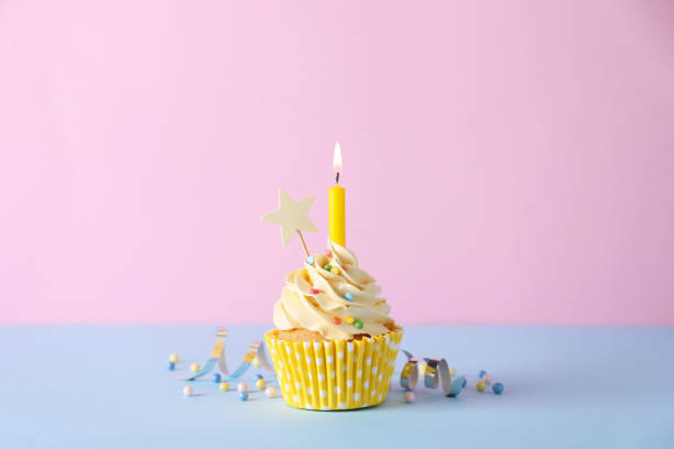 istock Delicious birthday cupcake with burning candle, sprinkles and streamer on light blue table against pink background 1464770221