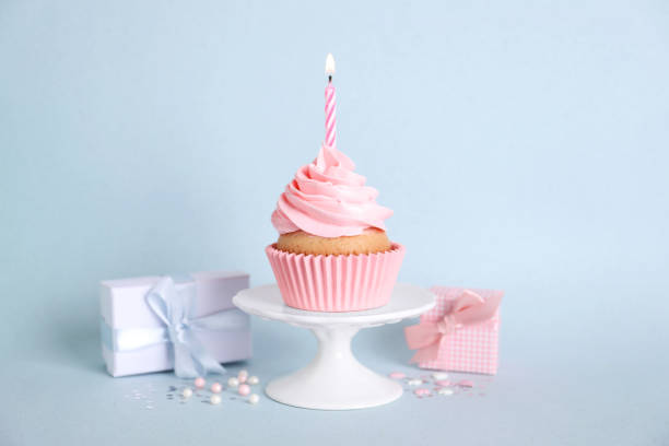 istock Delicious birthday cupcake with burning candle, sprinkles and gift boxes on light blue background 1464770225