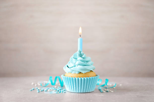 istock Delicious birthday cupcake with burning candle, sprinkles and streamer on grey table 1464770258