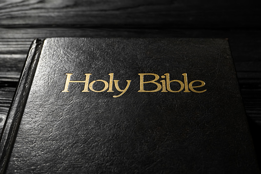 Bible with dark cover on black wooden table, closeup. Christian religious book