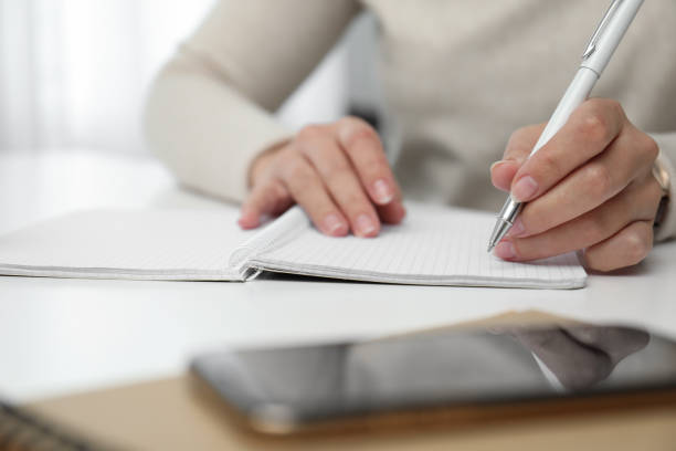 istock Left-handed woman writing in notebook at table indoors, closeup 1464772338