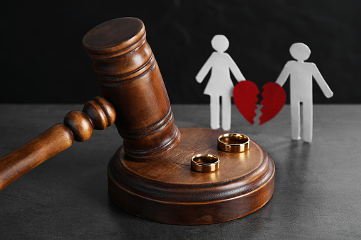 Divorce concept. Wooden gavel, wedding rings and paper cutout of couple with broken red heart on grey table