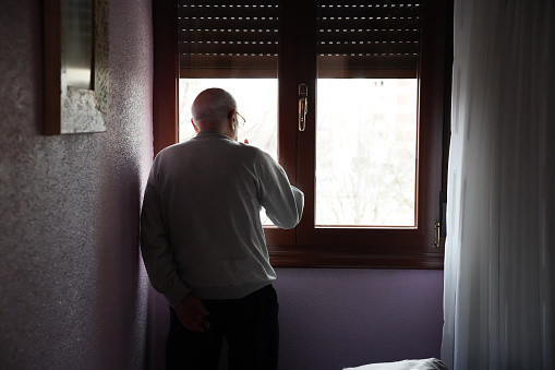 old man looking out the window in his bedroom. loneliness in old age