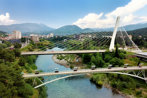 Aerial drone view of cable stayed Millennium bridge, footpath bridge and Moraca river in Podgorica, Montenegro on the background of amazing mountains.