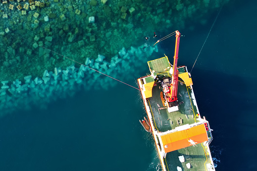 Drone view of a ship in the Adriatic Sea during the construction of a dam in the Lustica Bay near Tivat, Montenegro. Divers can be seen through the water, who strengthen the bottom with stone blocks.