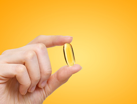 Woman hand holds yellow capsules of omega 3 on yellow background, healthy supplement pills.