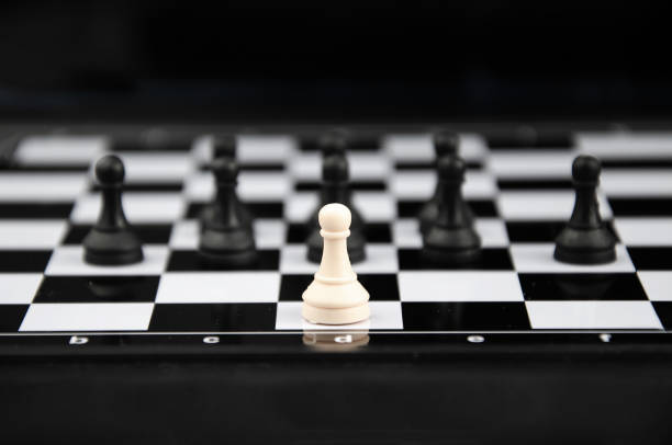 pezzo degli scacchi pedone bianco si trova sul bordo della scacchiera sullo sfondo del gruppo di pezzi neri - chess positioning strategy individuality foto e immagini stock