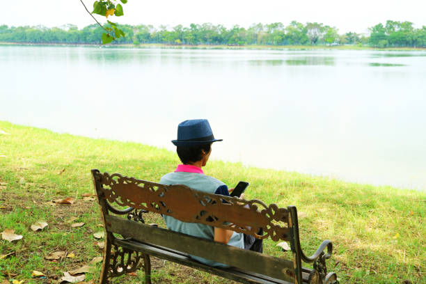 istock Man Sitting on the Lakeshore Bench Checking on His Smartphone 1464781387