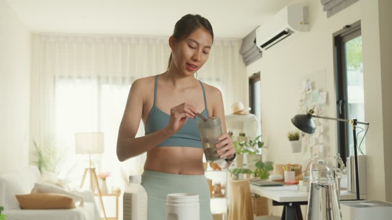 Young Asian athletic woman preparing protein shake at home. Diet and healthy food.