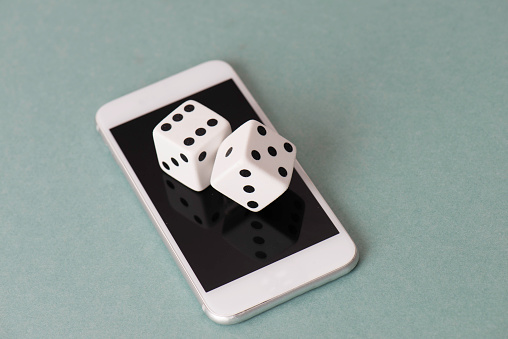Online gambling concept. Dice with white smart phone on the green background.