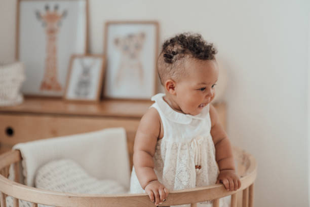 Portrait of mixed race toddler girl in round wooden baby crib at cozy childrens room neutral tones