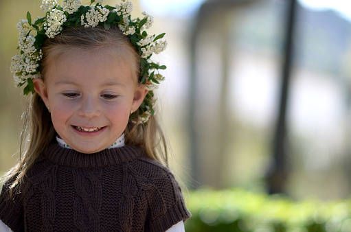 Girl in the park on sunny day with a wreath of white spring flowers on her head