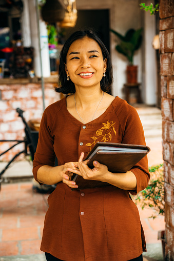 Smiling vietnamese Restaurant Owner with menu in her hands and looking at camera