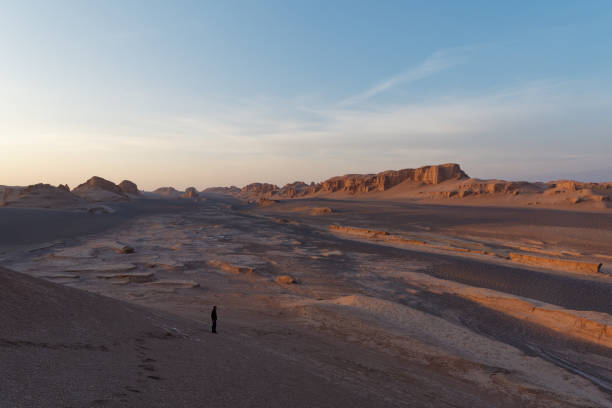 istock Serene sunset over the amazing Dasht-e Lut Desert and its rock formations (Kaluts) at sunset and silhouette of a man standing in the desert, Kerman Province, Iran 1464790268