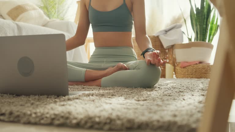 Closeup of young Asian athletic woman sportive top and leggings practicing yoga and listens spiritual practices lessons on laptop computer in living room at home. Diet and healthy weight loss.