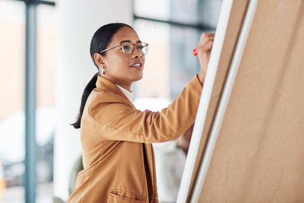 Creative woman, meeting and writing on Flipchart for team building, coaching or activity ideas at office. Happy female employee in presentation using board to write idea or FAQ for company startup