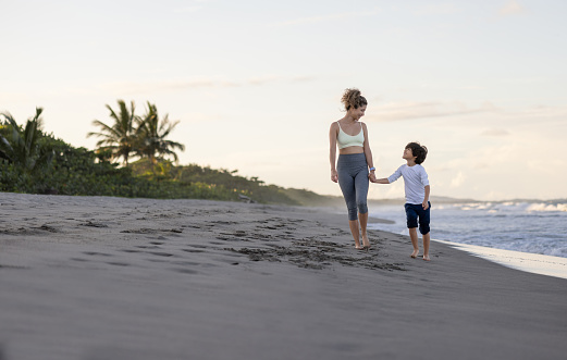 Loving Latin American mother and son walking together at the beach and holding hands