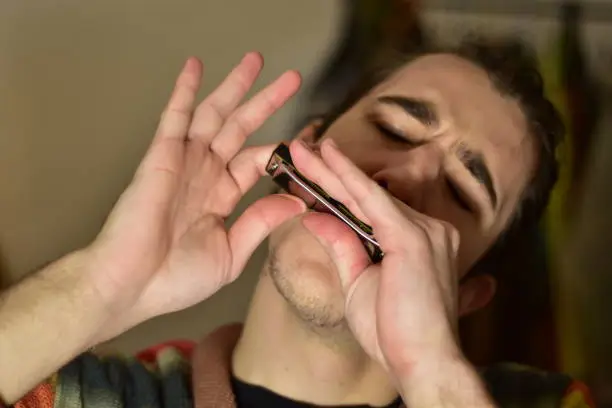 White Caucasian male playing harmonica at home passionately