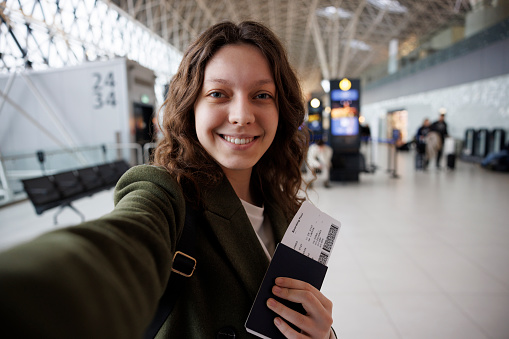 Excited teenage girl making selfie with passport and tickets at the airport