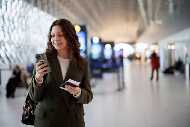 istock Smiling young woman using mobile phone at airport 1464801026