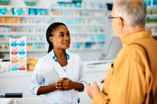 Young African American pharmacist talking to senior customer in a pharmacy,