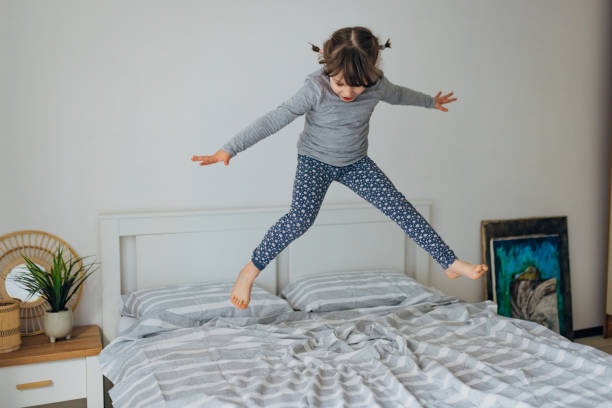 istock Playful little girl having fun while jumping on a bed in bedroom. Copy space 1464802880