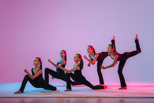 group of five teenagers balrins in black tight-fitting costumes are dancing modern konteporari on a lilac background