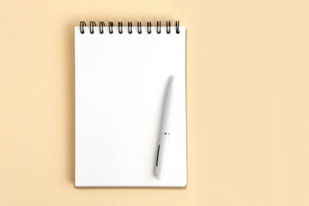 Notebook and pen. Spiral notepad on neutral beige color studio background. Top view. Open pad with blank white page. Greeting card mockup. Paper mock up. Modern Minimal business brand template. A6