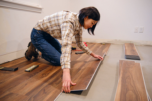 A woman installing laminate flooring in her home.