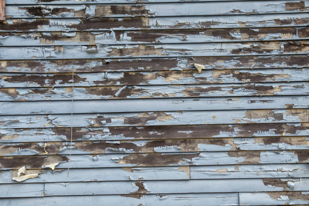 Background texture of pale blue peeling paint on a wood exterior wall.
