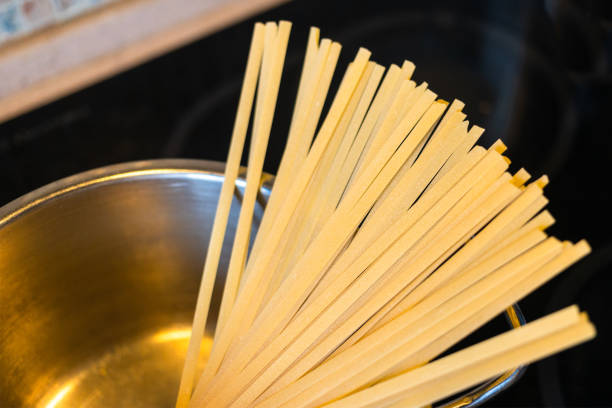 portion of uncooked linguine pasta closeup in saucepan at stove in home kitchen