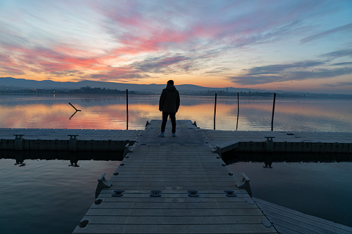 Sunrise over misty, foggy lake, with silhouetted figure, man walking down dock, pier. magical perspective with beautiful orange sunrise filtering through rising mist from a calm