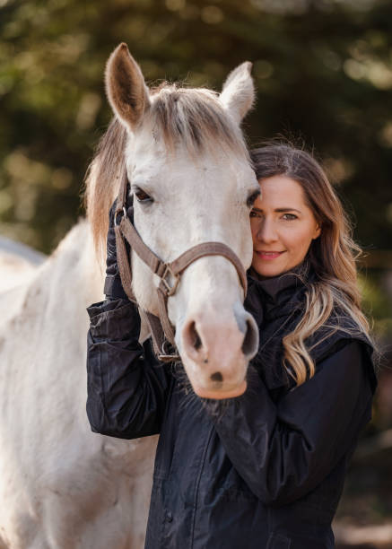 白いアラビアの馬の隣に立つ若い女性、ぼやけた木の背景、クローズアップの詳細 - horse arabian horse arabia white ストックフォトと画像