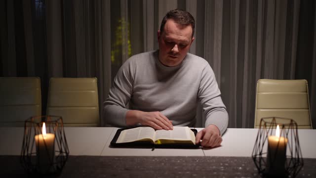 The man lit candles at the table and reads the Bible